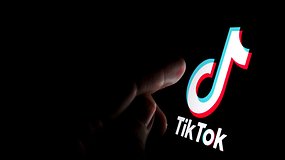 Ein Finger tippt vor schwarzem Hintergrund auf ein Handy-Display, auf dem man groß das TikTok-Logo sieht