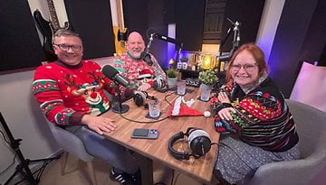 Johanna, Fabi und Casi sitzen zusammen in einem Podcast-Studio und tragen Weihnachtspullover