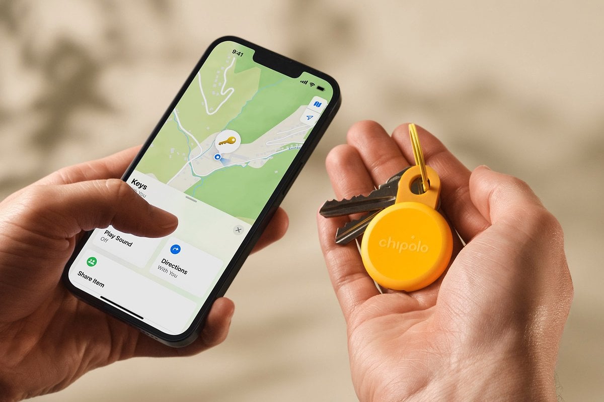 Une main tenant un smartphone affichant une carte avec un tracker Chipolo Loop et des clés.