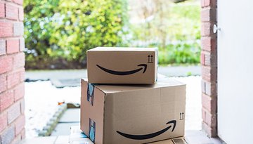 Amazon-Pakete liegen vor einer offenen Haustür auf der Matte