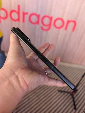 A person holding an Asus ROG Phone 9, showcasing its slim profile against a pink Snapdragon backdrop.