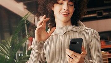 Uma pessoa com cabelo cacheado segura um smartphone Google Pixel 9a e sorri enquanto interage com ele.