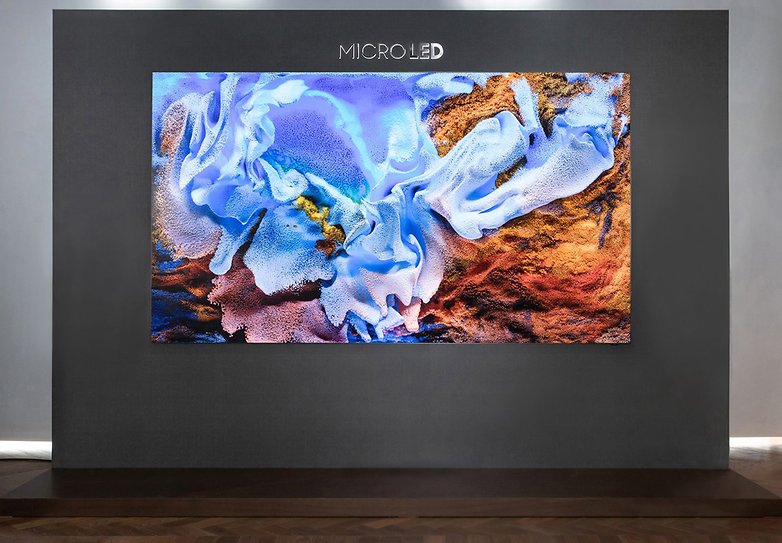 Uma grande TV Samsung MicroLED exibindo uma obra de arte abstrata azul e dourada em uma parede cinza.