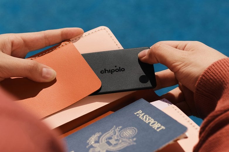 A person holds a Chipolo card item tracker in their hand, next to a passport and wallet. A person holds a Chipolo card item tracker in their hand, next to a passport and wallet.
