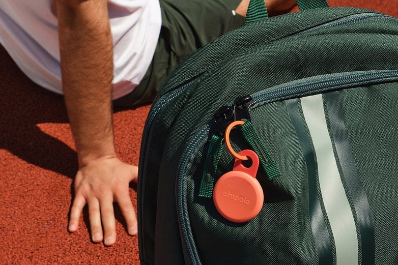 A Chipolo Loop item tracker attached to a green backpack on a red surface. A Chipolo Loop item tracker attached to a green backpack on a red surface.