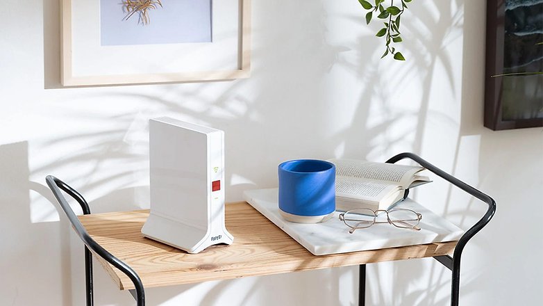 Ein Fritz-Repeater auf einem Holztisch mit einer blauen Tasse, einem Buch und einer Brille. Ein Fritz-Repeater auf einem Holztisch mit einer blauen Tasse, einem Buch und einer Brille.