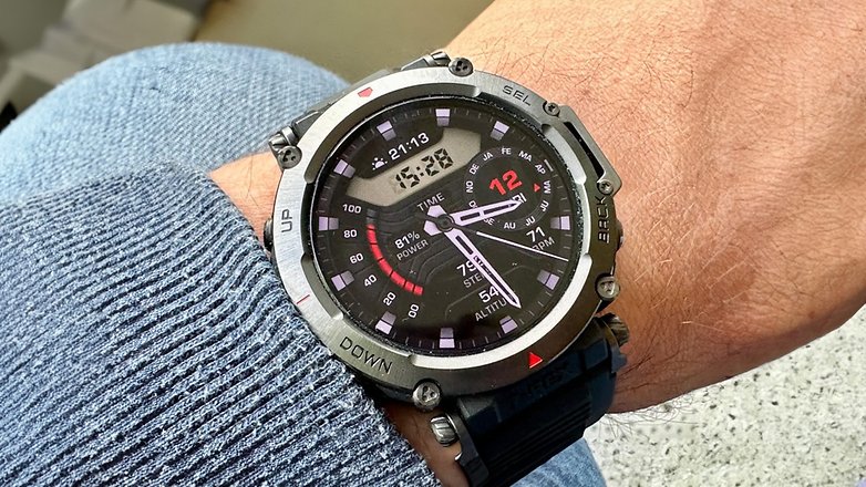 Amazfit T-Rex Ultra Smartwatch an einem Handgelenk, das die Uhrzeit und verschiedene Fitnessmetriken anzeigt. Amazfit T-Rex Ultra Smartwatch an einem Handgelenk, das die Uhrzeit und verschiedene Fitnessmetriken anzeigt.