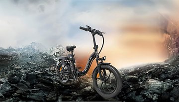 Ein schwarzes Avaka-E-Bike steht auf steinigem Terrain mit Bergen im Hintergrund.
