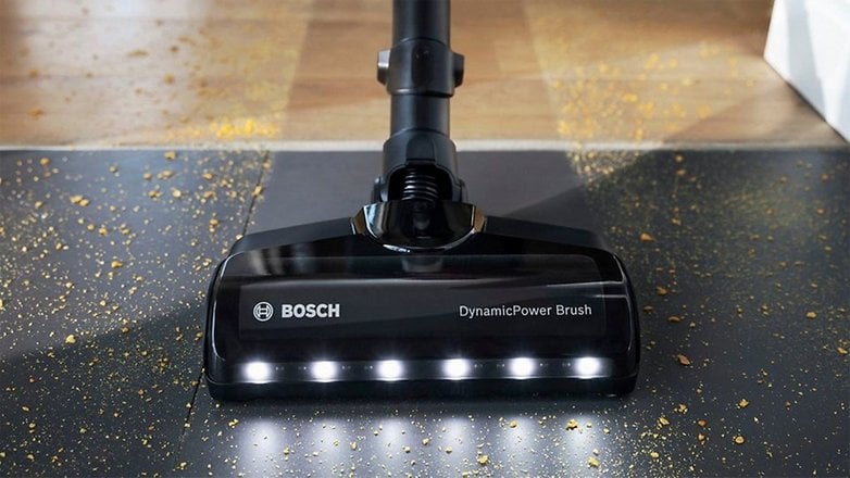 Bosch Staubsaugerkopf mit DynamicPower-Bürste und LED-Lichtern auf einer Oberfläche mit verstreutem Schmutz.