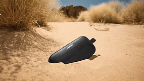 Bose SoundLink Flex 2. Generation Lautsprecher, der im Sand mit spärlicher Vegetation im Hintergrund liegt.