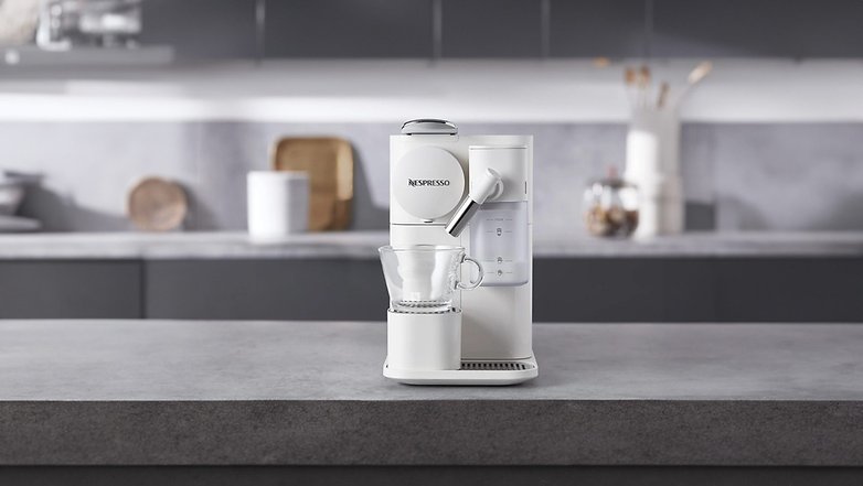 Delonghi Lattissima One Kaffeemaschine in Weiß auf einer Arbeitsplatte mit einer Glastasse. Delonghi Lattissima One Kaffeemaschine in Weiß auf einer Arbeitsplatte mit einer Glastasse.