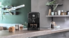 Kaffeevollautomat De'Longhi Magnifica S auf einer Küchenarbeitsplatte mit zwei Tassen Kaffee und einem Gebäck.