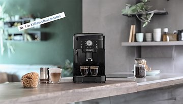 Kaffeevollautomat De'Longhi Magnifica S auf einer Küchenarbeitsplatte mit zwei Tassen Kaffee und einem Gebäck.