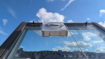 Ein Fensterputzroboter auf einer Glasfläche unter einem blauen Himmel.