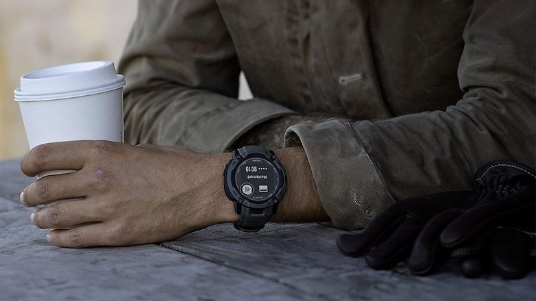 Eine Person hält einen Kaffeebecher mit einer Garmin Instinct 2X Solar Uhr am Handgelenk.