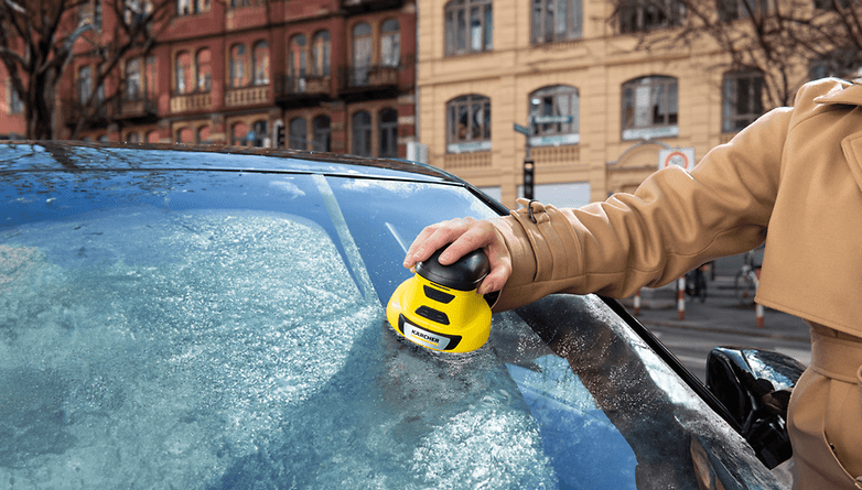 Eine Person benutzt ein Kärcher-Gerät, um Eis von einer Autoscheibe in einer städtischen Umgebung zu entfernen.