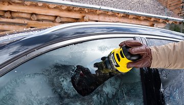 Eine Person verwendet einen Kärcher-Eiskratzer an einem gefrorenen Autofenster.