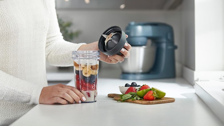 Eine Person bereitet einen Smoothie mit Früchten in einem Mixer vor, mit einer Kenwood-Küchenmaschine im Hintergrund. Eine Person bereitet einen Smoothie mit Früchten in einem Mixer vor, mit einer Kenwood-Küchenmaschine im Hintergrund.