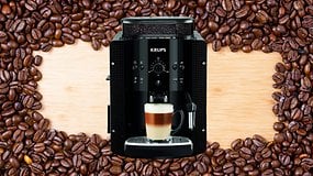 Eine schwarze KRUPS EA8108 Kaffeemaschine mit einem geschichteten Kaffeegetränk davor, umgeben von Kaffeebohnen auf einem Holzuntergrund.