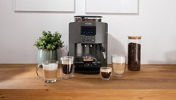 Eine Krups Essential EA8100 Kaffeemaschine mit verschiedenen Kaffeegetränken auf einem Holztisch.