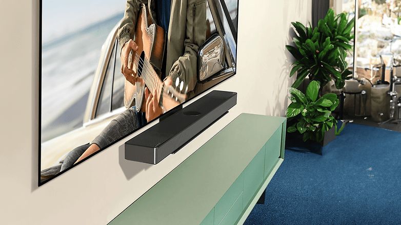 Ein schlanker LG C4 OLED Evo TV an der Wand montiert mit einer Soundbar darunter und daneben Topfpflanzen.