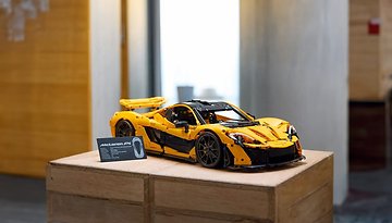 Ein LEGO-Modell eines McLaren P1, auf einer Holzbox mit einer Informationskarte ausgestellt.