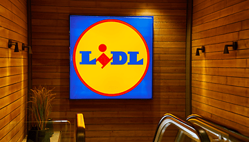 Beleuchtetes Lidl-Logo an einer Holzwand mit angrenzenden Rolltreppen.