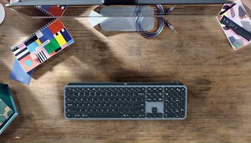 Überhead-Ansicht einer Logitech MX Keys Mini-Tastatur auf einem Holztisch, umgeben von Notizbüchern und Schreibwaren.