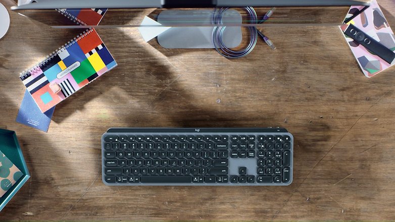 Überhead-Ansicht einer Logitech MX Keys Mini-Tastatur auf einem Holztisch, umgeben von Notizbüchern und Schreibwaren.