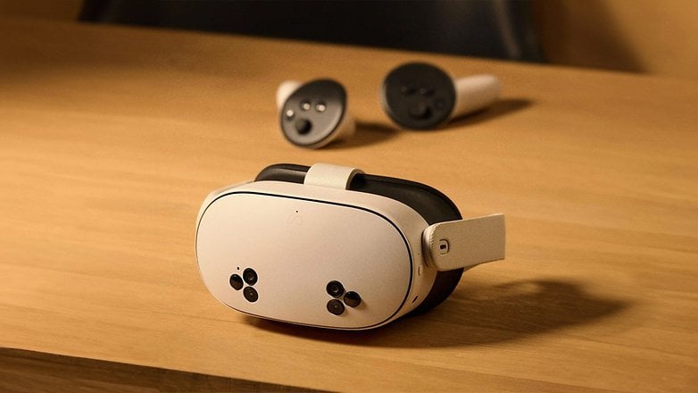 Ein Meta Quest 3S VR-Headset auf einer Holzoberfläche mit zwei Controllern im Hintergrund. Ein Meta Quest 3S VR-Headset auf einer Holzoberfläche mit zwei Controllern im Hintergrund.