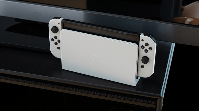 Eine Nintendo Switch OLED-Konsole in Weiß, auf einem schwarzen Regal platziert.