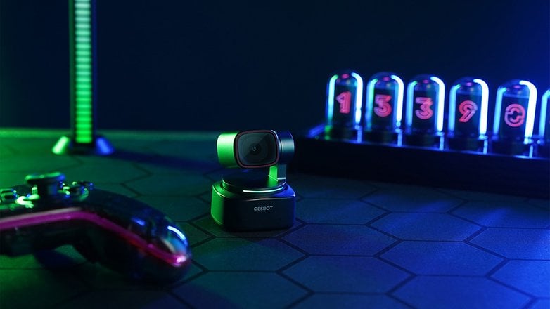 Eine schwarze OBSBOT Tiny 2 Kamera auf einer sechseckigen Fläche mit einem Gaming-Controller und Neon-Zahlendisplays im Hintergrund. Eine schwarze OBSBOT Tiny 2 Kamera auf einer sechseckigen Fläche mit einem Gaming-Controller und Neon-Zahlendisplays im Hintergrund.