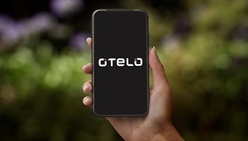 Eine Hand hält ein Smartphone, das das Otelo-Logo auf dunklem Hintergrund zeigt.