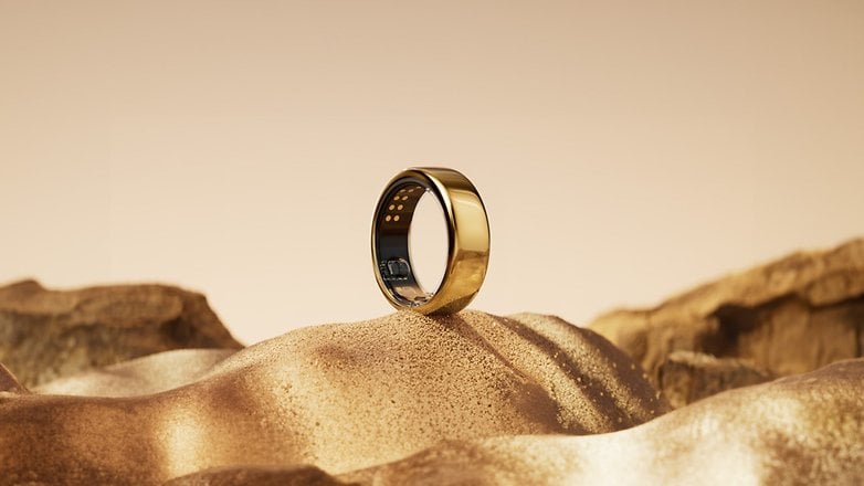 Ein goldener Smart-Ring ruht auf einer sandigen Oberfläche mit einem sanften Farbverlauf im Hintergrund. Ein goldener Smart-Ring ruht auf einer sandigen Oberfläche mit einem sanften Farbverlauf im Hintergrund.