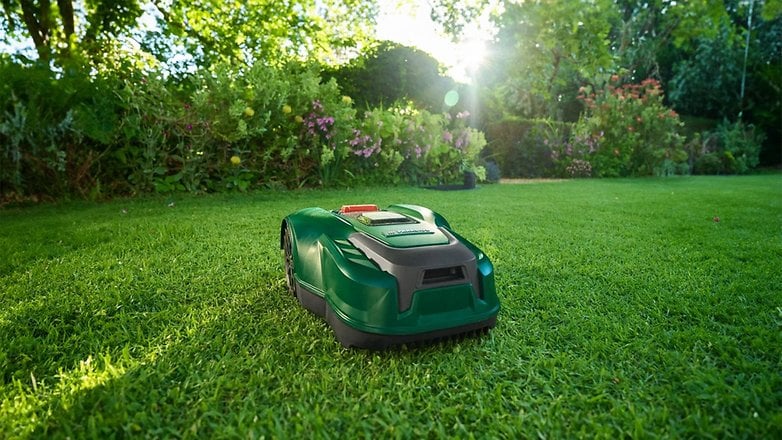 Ein grüner Mähroboter auf einem gepflegten Rasen, umgeben von Blumen. Ein grüner Mähroboter auf einem gepflegten Rasen, umgeben von Blumen.