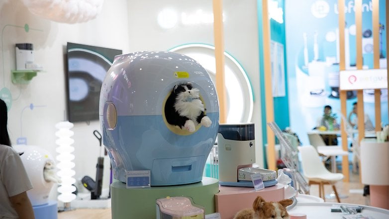 Eine Katze schaut aus einem stilvollen Tierhaus an einem Technik-Messe-Stand heraus. Eine Katze schaut aus einem stilvollen Tierhaus an einem Technik-Messe-Stand heraus.
