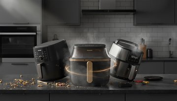 Drei Heißluftfritteusen auf einer Küchentheke, darunter ein Philips- und ein Ninja-Modell, mit verstreuten Kochzutaten.