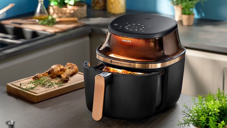 Philips-Heißluftfritteuse mit transparentem Deckel, gekochtem Hähnchen und Kräutern auf einer Küchenarbeitsplatte.