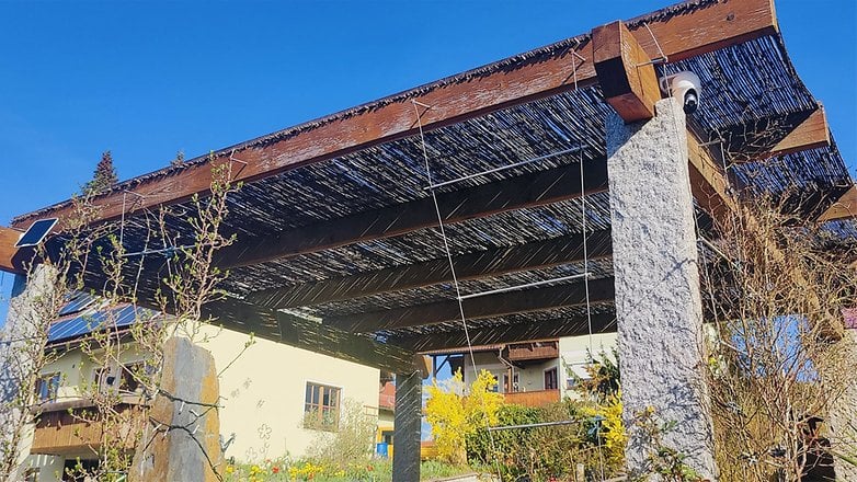 Eine Holzstruktur mit einem Reetdach und einer Sicherheitskamera, umgeben von blühenden Pflanzen. Eine Holzstruktur mit einem Reetdach und einer Sicherheitskamera, umgeben von blühenden Pflanzen.