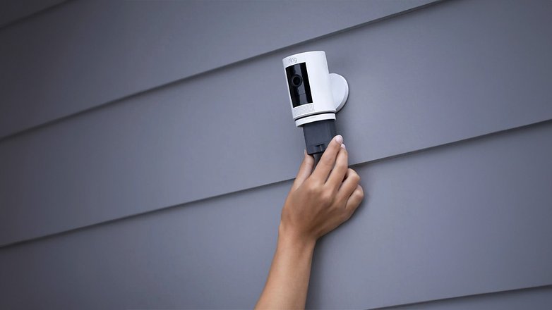 Eine Hand installiert eine Ring-Sicherheitskamera an einer grauen Wand. Eine Hand installiert eine Ring-Sicherheitskamera an einer grauen Wand.