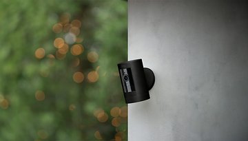 Eine schwarze Ring-Sicherheitskamera, die an einer Wand montiert ist, vor einem unscharfen grünen Hintergrund.