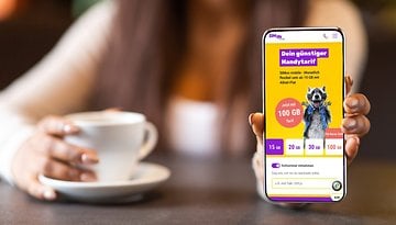 Eine Person hält ein Smartphone, das die Mobilfunktarife von SIMon mobile anzeigt, mit einer Tasse Kaffee im Hintergrund.