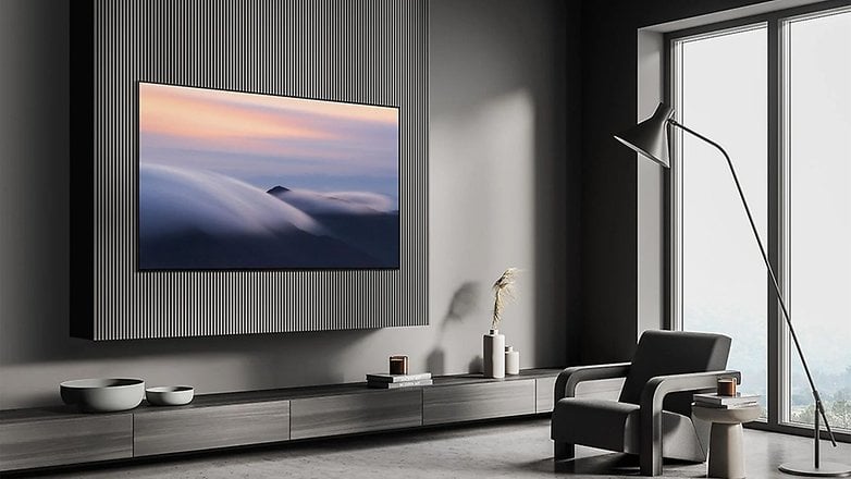 Ein schlanker Samsung S90D Fernseher, der an einer strukturierten Wand in einem modernen Wohnzimmer montiert ist, mit einem stilvollen Sessel.