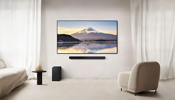 Ein modernes Wohnzimmer mit einer Samsung-Soundbar unter einem Fernseher, der eine Berglandschaft zeigt.