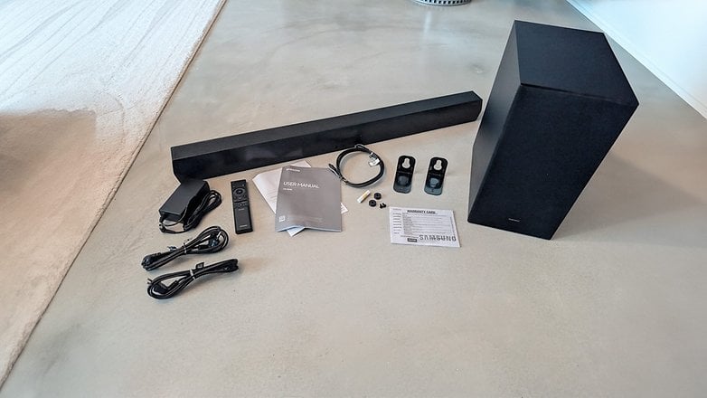 Samsung HW-B540 Soundbar und Subwoofer mit Fernbedienung, Kabeln und Benutzerhandbuch auf einer Fläche.