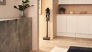Ein kabelloser Samsung-Staubsauger steht an einer Wand in einem modernen Raum mit hellem Holzfußboden.
