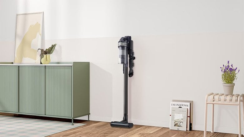 Ein kabelloser Staubsauger von Samsung an der Wand neben einem grünen Schrank und dekorativen Gegenständen. Ein kabelloser Staubsauger von Samsung an der Wand neben einem grünen Schrank und dekorativen Gegenständen.