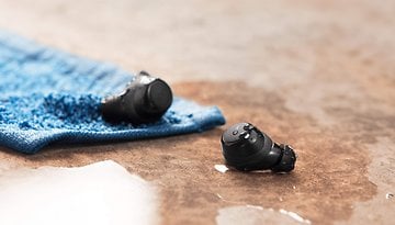 Schwarze In-Ear-Sportkopfhörer mit Wassertropfen auf einem blauen Handtuch.