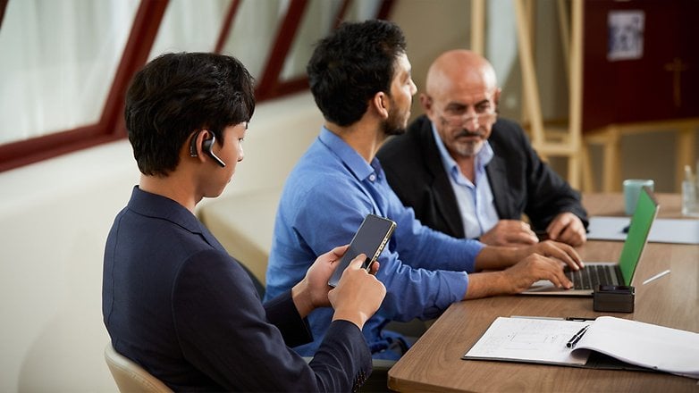 Trois hommes en réunion, l'un au téléphone, utilisant le Timekettle W4 Pro pour communiquer.