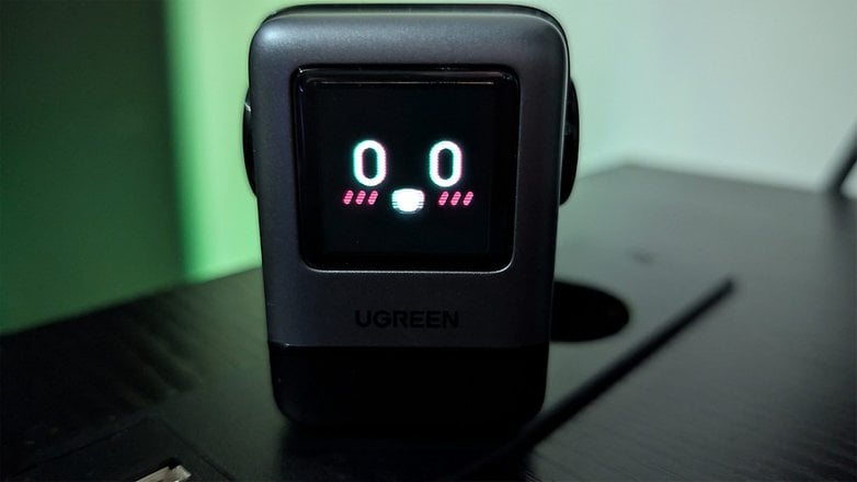 A Ugreen Uno 100W charger with a digital display showing '00' and a smiling face.